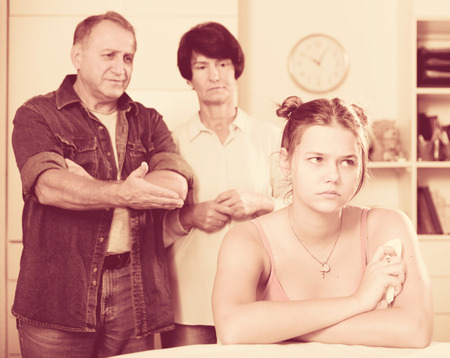 Parents are sympathying their sad daughter who is sitting at the table at home.の写真素材