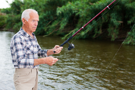 Positive adult man with rod relaxing and enjoying fishing by lakesideの写真素材