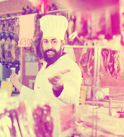 Smiling positive man seller showing sorts of meat in butcherâs shopの写真素材