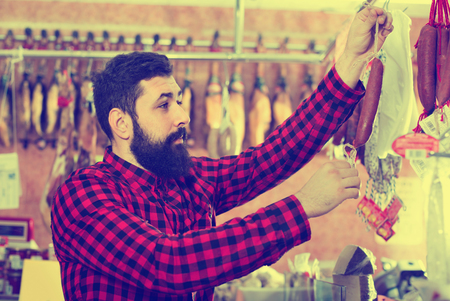 Young smiling male customer examining sausages in butcherâs shopの写真素材