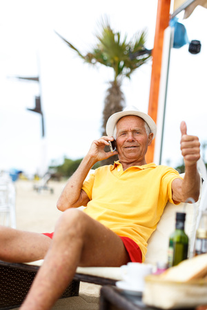 Satisfied elderly man resting near ocean and speaking phoneの写真素材
