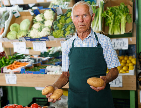 Friendly older man seller proffering fresh organic fruits and vegetables in supermarketの写真素材