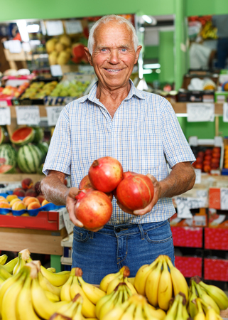 Positive aged male customer searching for fresh fruits in greengroceryの写真素材