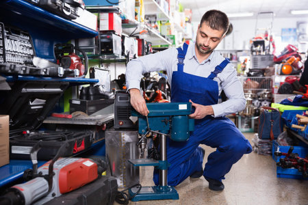 Efficient glad friendly male is standing with drilling machine in tools store.