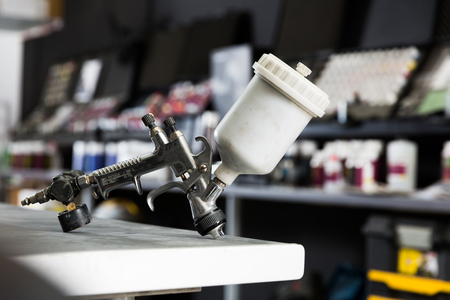 Closeup of paint-spray gun on table in professional car painting workshopの写真素材