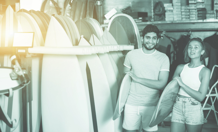 Happy cheerful positive couple of positive man with boards for surfing in the shopの写真素材