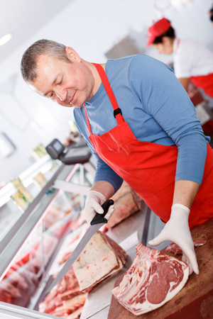 Smiling man  seller cutting meat in butcherâs shopの写真素材