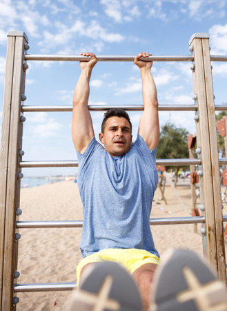 Athletic male doing workout on fitness station exercising in morning outdoors