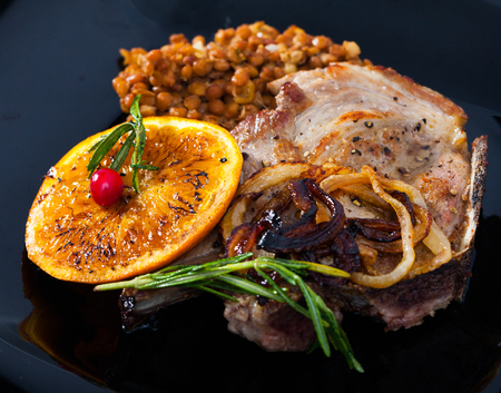 Cooked pork loin chops with lentils and grilled orange garnished with rosemary and onionの写真素材