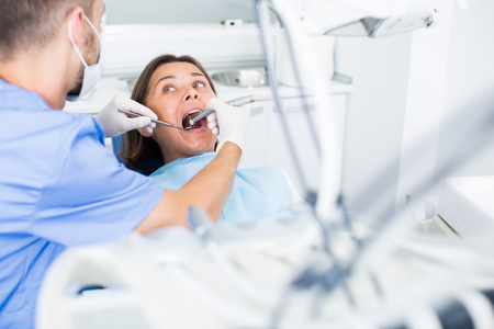 male Dentist is treating patient which is sitting in dental chair in clinicの写真素材