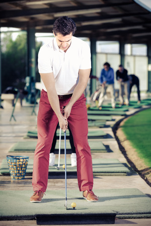 Smiling male golfer getting ready to hit ball at golf courseの写真素材