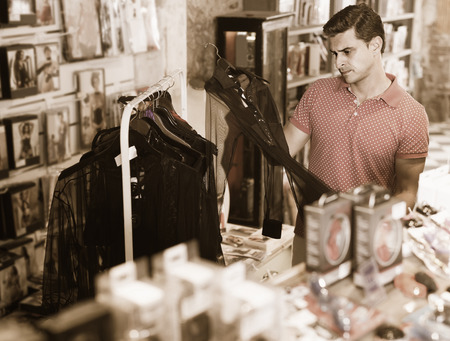 Buyer spanish adult man choosing black sexual shirt in the sex shopの写真素材