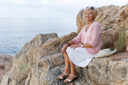 Happy senior woman sitting at seaside and admiring natureの写真素材