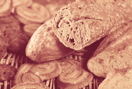 Closeup of cut wholegrain baguette with various bakery products on wicker matの写真素材