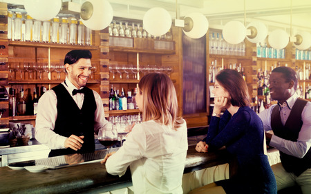 Happy cheerful positive smiling barman is servicing young people who are relaxing in bar indoor.の写真素材