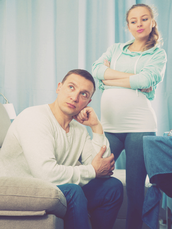 Middle-aged husband and pregnant wife arguing with each other at homeの写真素材