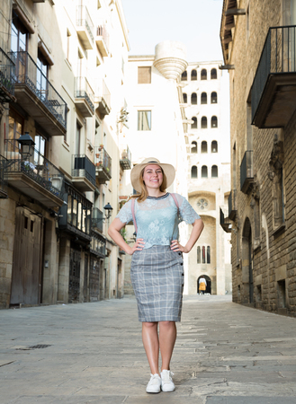 Portrait of young positive female in hat standing in the historical city centerの写真素材
