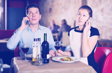 Elegant couple emotionally speaking on phones at restaurantの写真素材