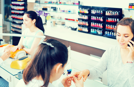woman getting manicure in beauty salon and talking on phone during the procedureの写真素材