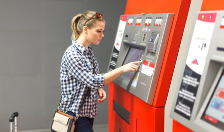 Adult woman traveler with red suitcase buying ticket in subway at ticket vending machine