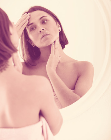 Young woman checking her face in mirror in morningの写真素材