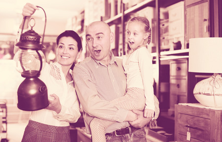 Positive couple with their daughter are choosing lamp in furniture shopの写真素材