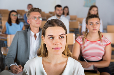 Intelligent girl listening with attention during classes in auditorium among her fellow studentsの写真素材