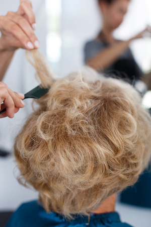 Closeup of hands of professional hairdresser making hairstyle for female client in hair studioの写真素材