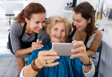 Professional hairstylists and satisfied female customer taking selfie after haircut in modern hair...