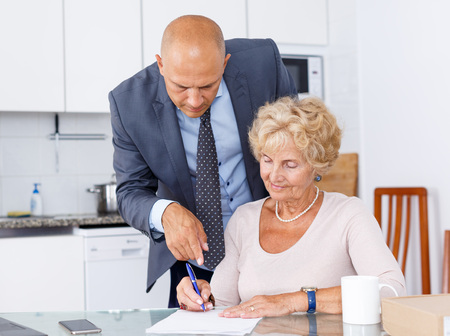 Sales agent helping to elderly woman fill out purchase order in kitchenの写真素材