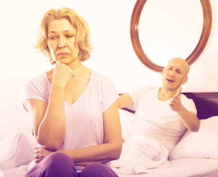 Aged man and frustrated  elderly woman sorting out relationships in bedの写真素材