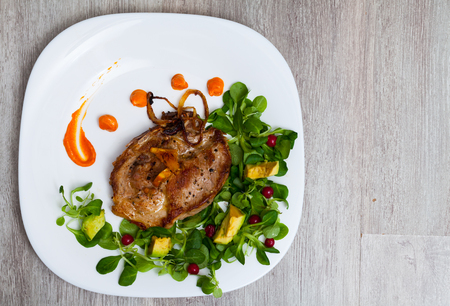 Top view of fried pork chop with pumpkin puree and salad from avocado, cornsalad and redcurrant berries on wooden backgroundの写真素材