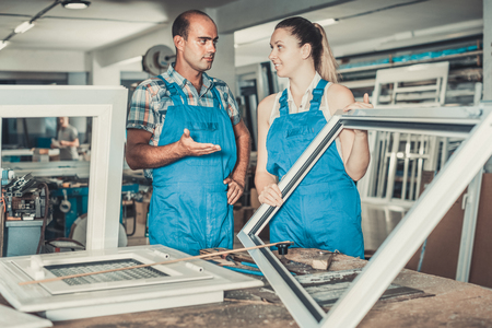 Man worker helping female in work of assembling plastic windows at factoryの写真素材