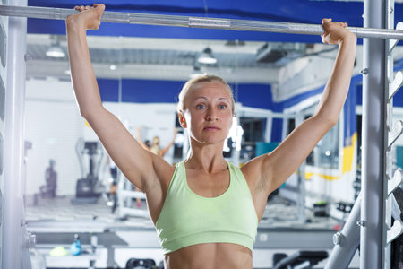 Athletic woman performing weightlifting workout at gym, exercising with barbell