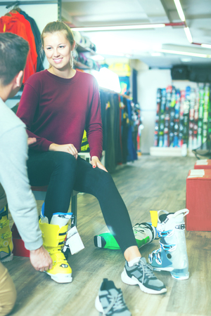 Seller is helping glad young girl to trying on ski boots in sport shop.の写真素材