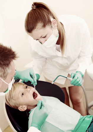 Stomatologist guy with female assistant are diagnosticating to young patient which is sitting in dental clinic.の写真素材