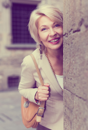 Adult woman is posing in time wallking near old wall in city.の写真素材