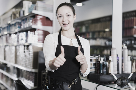 Portrait of professional positive female hairdresser holding thumbs up in salonの写真素材