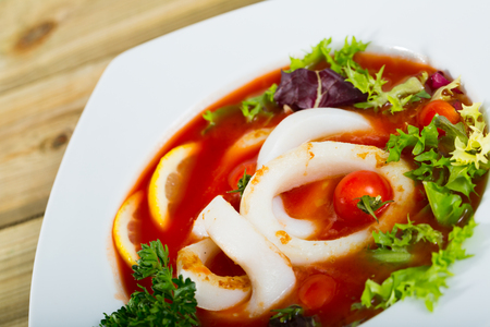 Beautifully served bowl with tomato soup with squid and greensの写真素材