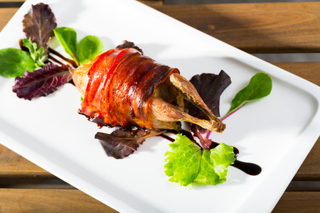 Image of baked in bacon quail with balsamic sauce on the plate indoors.の写真素材