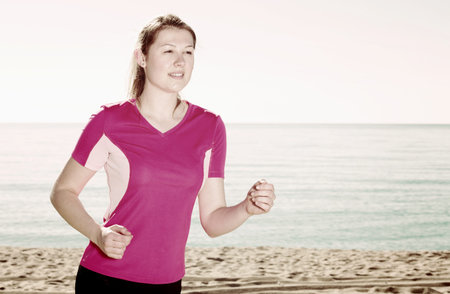 Young sporty woman running on ocean beach in sunny morning