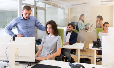 Chief executive explaining task to female coworker, pointing at computer screen in modern office