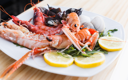 White plate with cooked shrimps, langoustines, clams with herb and lemon slices on wooden backgroundの写真素材