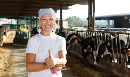 Smiling mature female proffesional farmer  standing near cows  at  farmの写真素材