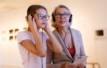 Attentive tween girl with senior woman exploring art museum on self-guided tour