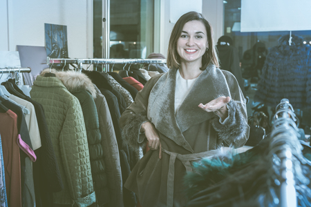 Attractive girl customer deciding on the choice of sheepskin coat in womenâs cloths shopの写真素材
