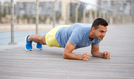 Young sporty male doing workout on seashore at sunny morning