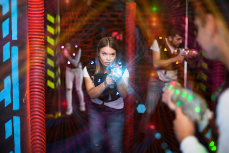 Portrait of girl in colored beams of laser guns during laser tag game on dark arenaの写真素材
