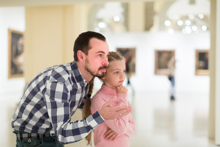 Smiling father and small daughter exploring paintings in halls of museumの写真素材