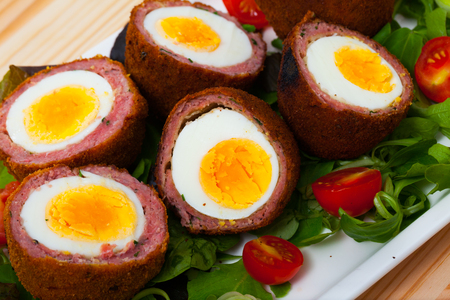 Scottish cuisine. Hard-boiled eggs wrapped in sausage meat, breaded and fried (Scotch eggs) served with mix of greens and cherry tomatoesの写真素材